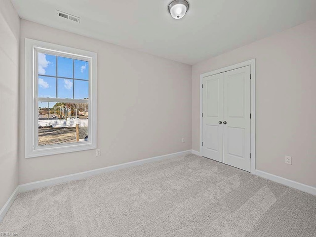 unfurnished bedroom featuring baseboards, visible vents, a closet, and light colored carpet