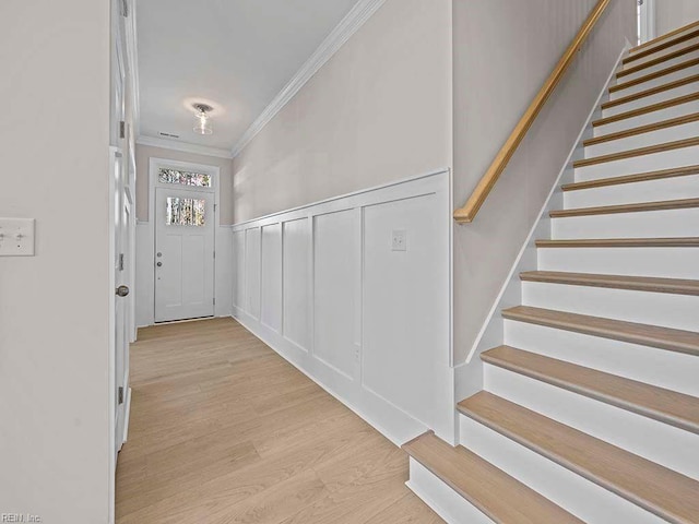 entrance foyer with a wainscoted wall, stairs, crown molding, light wood-style floors, and a decorative wall