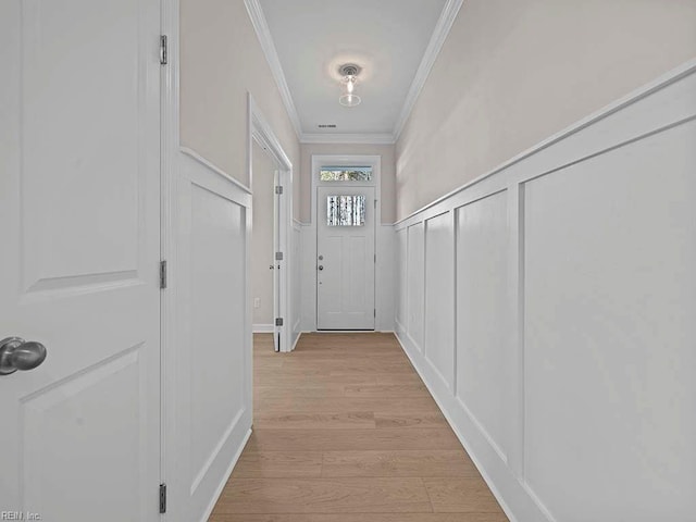 entryway featuring light wood finished floors, ornamental molding, a decorative wall, and wainscoting