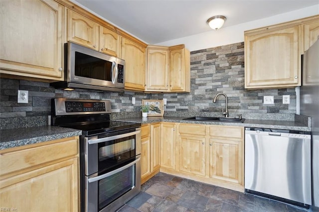 kitchen with stone finish floor, appliances with stainless steel finishes, a sink, light brown cabinets, and backsplash