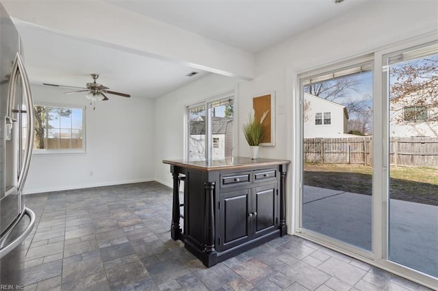 kitchen with visible vents, baseboards, dark cabinetry, stainless steel fridge with ice dispenser, and stone finish floor