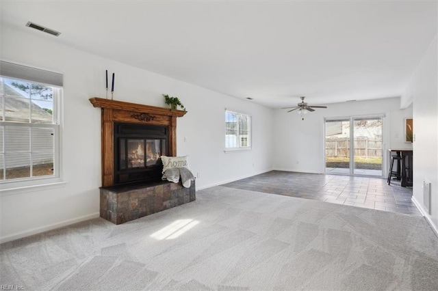 unfurnished living room featuring carpet floors, visible vents, a ceiling fan, a glass covered fireplace, and baseboards