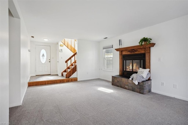 unfurnished living room featuring carpet, stairway, baseboards, and a glass covered fireplace