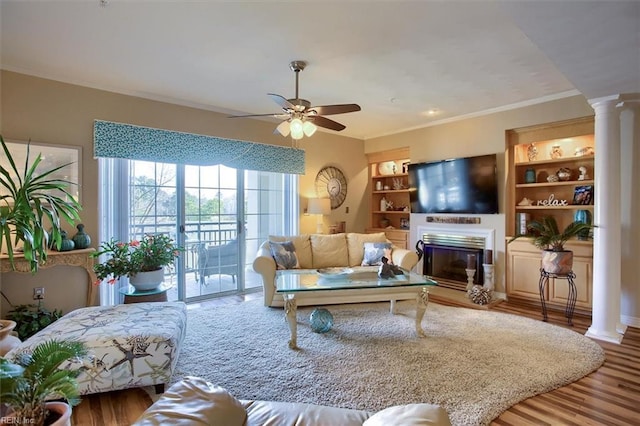 living room featuring ornate columns, ornamental molding, wood finished floors, and a glass covered fireplace