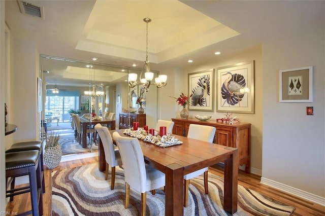 dining room featuring a raised ceiling, visible vents, a notable chandelier, and wood finished floors