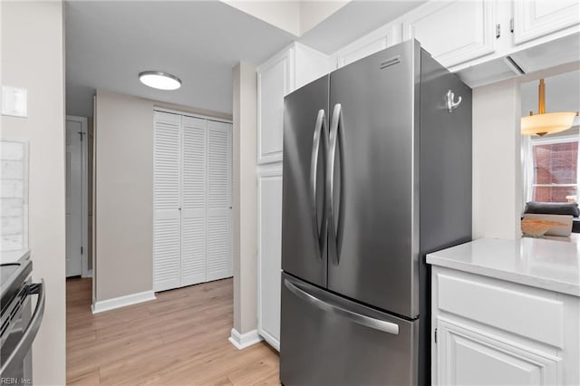 kitchen with light wood-type flooring, range, freestanding refrigerator, and white cabinetry