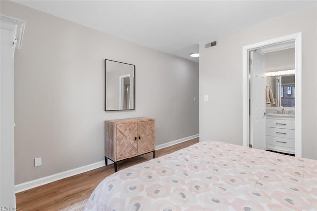 bedroom featuring baseboards, visible vents, wood finished floors, and ensuite bathroom