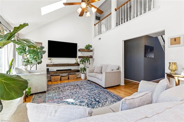 living area with ceiling fan, high vaulted ceiling, a skylight, and wood finished floors