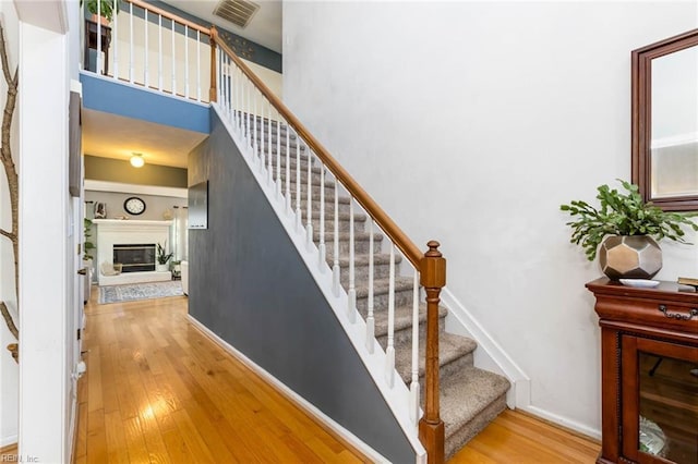 stairway featuring a towering ceiling, hardwood / wood-style flooring, a glass covered fireplace, and visible vents