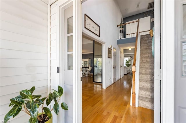 corridor featuring stairs, a high ceiling, light wood-type flooring, and visible vents