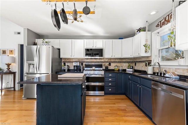 kitchen with stainless steel appliances, dark countertops, white cabinetry, a sink, and blue cabinets