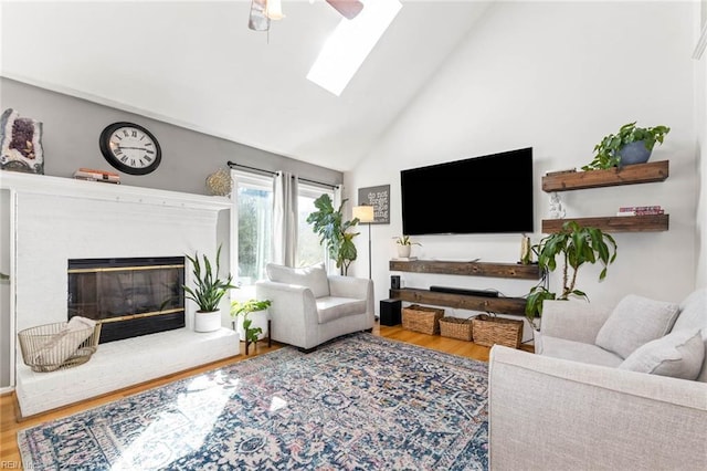 living room featuring a skylight, a ceiling fan, a glass covered fireplace, wood finished floors, and high vaulted ceiling