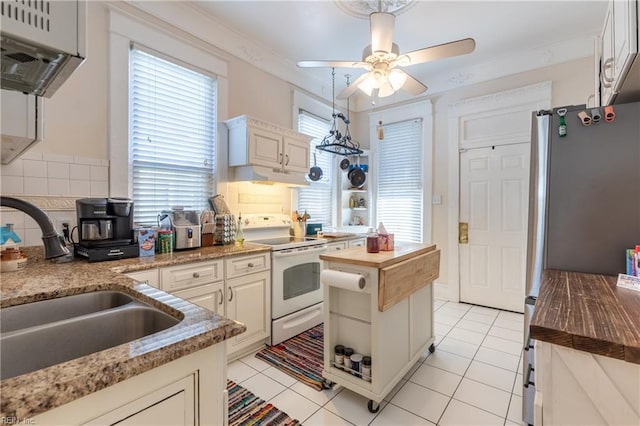 kitchen featuring electric stove, light tile patterned floors, freestanding refrigerator, a sink, and wood counters