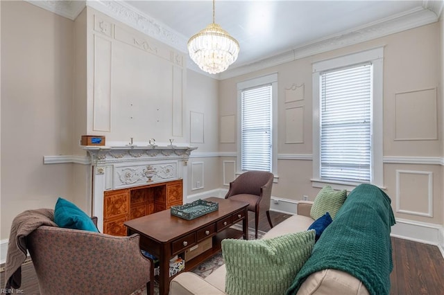 living area featuring baseboards, dark wood-style floors, ornamental molding, a chandelier, and a decorative wall