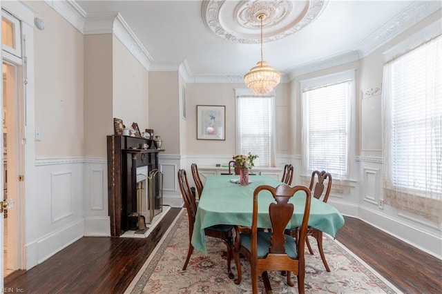 dining room featuring a wainscoted wall, a notable chandelier, a decorative wall, dark wood-type flooring, and ornamental molding