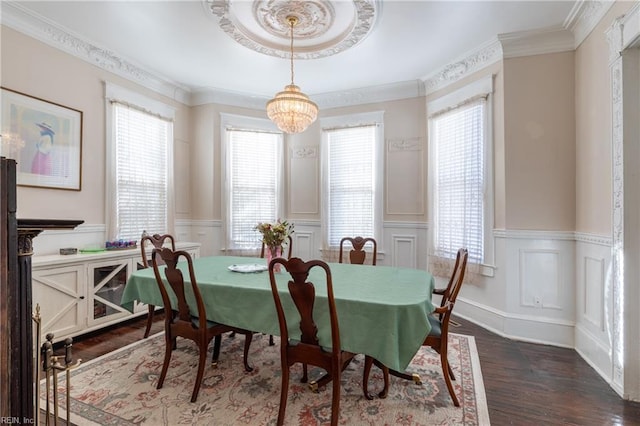 dining space with dark wood-style floors, an inviting chandelier, crown molding, and wainscoting