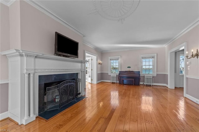 unfurnished living room featuring a fireplace with raised hearth, crown molding, radiator heating unit, and light wood-style floors