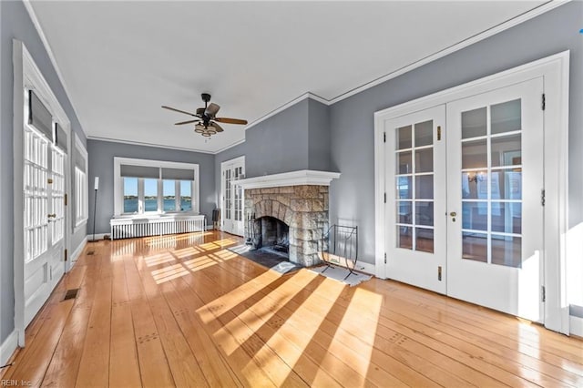 unfurnished living room with french doors, visible vents, ornamental molding, a stone fireplace, and hardwood / wood-style floors