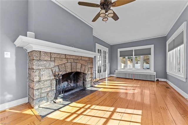 unfurnished living room featuring baseboards, radiator, wood-type flooring, crown molding, and a stone fireplace