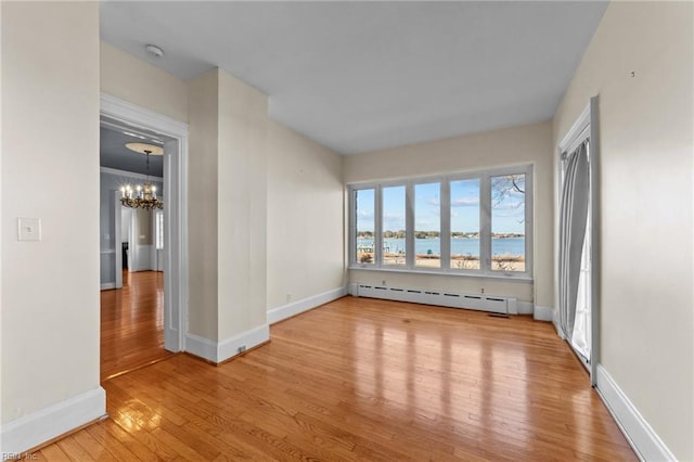 empty room with hardwood / wood-style flooring, a baseboard radiator, baseboards, and a notable chandelier