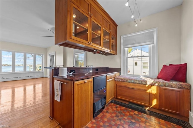 kitchen featuring a baseboard radiator, a peninsula, open floor plan, brown cabinetry, and glass insert cabinets