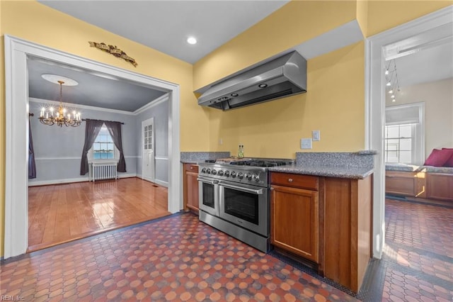 kitchen with a chandelier, double oven range, radiator, wall chimney exhaust hood, and brown cabinetry