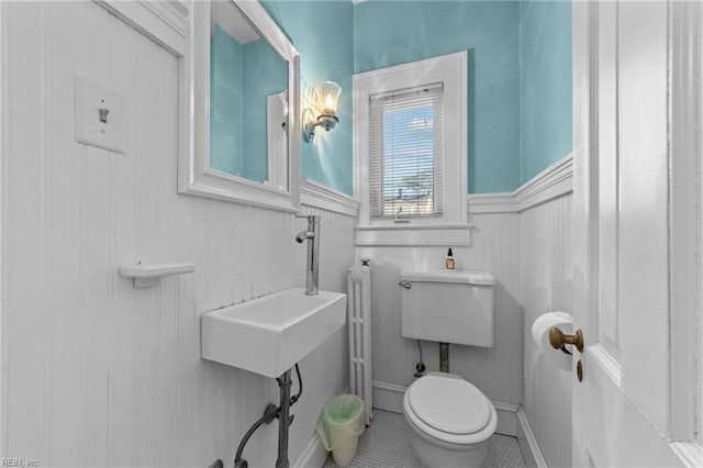 bathroom featuring toilet, tile patterned floors, a sink, and wainscoting