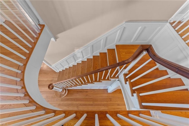 stairway with wainscoting, a decorative wall, and wood finished floors