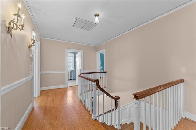 hall with ornamental molding, light wood finished floors, an upstairs landing, and baseboards