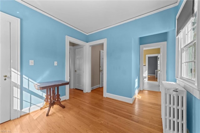 empty room with ornamental molding, radiator, light wood-style flooring, and baseboards