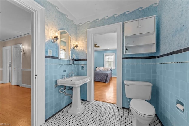 half bathroom featuring wallpapered walls, toilet, a wainscoted wall, crown molding, and tile walls