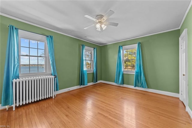 empty room with hardwood / wood-style floors, radiator heating unit, ornamental molding, a ceiling fan, and baseboards