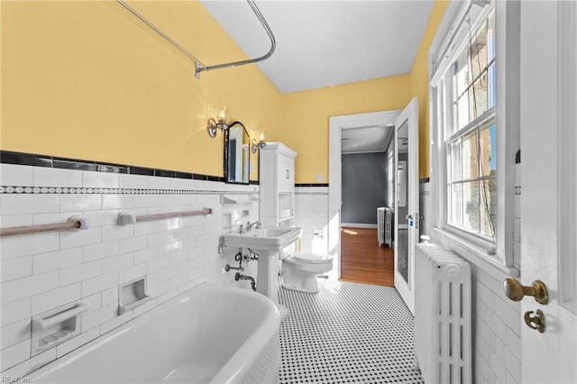 bathroom with radiator, a wainscoted wall, a bathing tub, and toilet