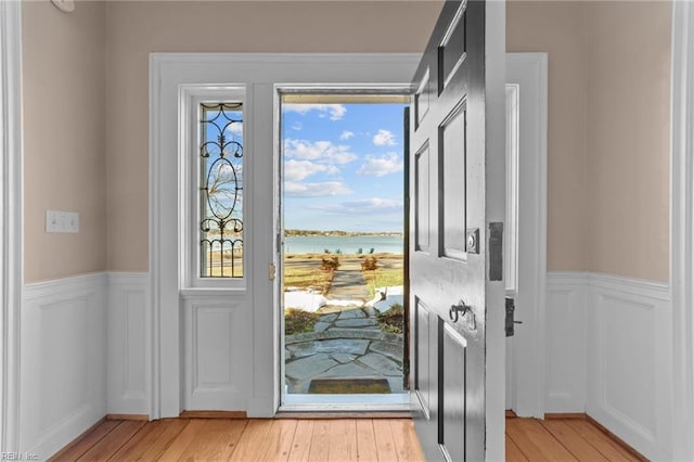 doorway featuring wainscoting, a decorative wall, a water view, and light wood-style floors