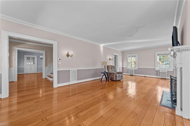 unfurnished room with crown molding, light wood finished floors, radiator, visible vents, and stairs