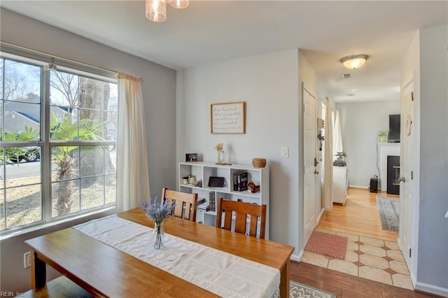 dining space featuring light wood finished floors, a glass covered fireplace, and baseboards