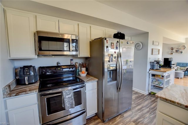 kitchen featuring baseboards, wood finished floors, light stone countertops, stainless steel appliances, and white cabinetry