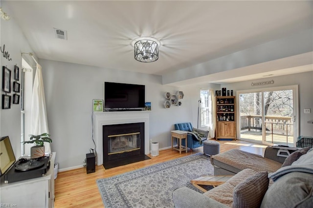 living area with light wood-style floors, a fireplace with flush hearth, visible vents, and baseboards