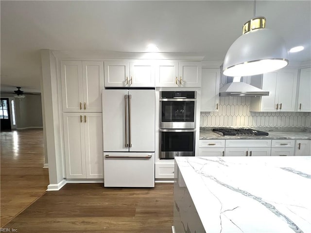 kitchen with stainless steel appliances, wall chimney exhaust hood, white cabinetry, and light stone counters