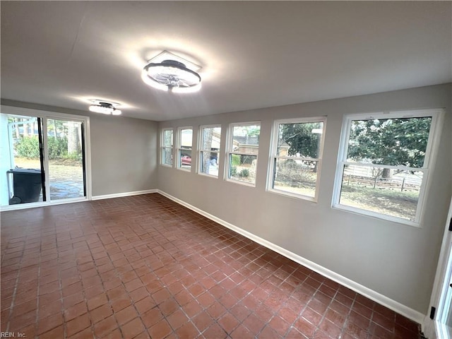 spare room with brick floor, a healthy amount of sunlight, and baseboards