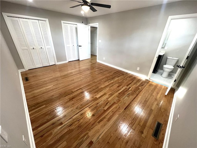 unfurnished bedroom featuring ensuite bathroom, wood finished floors, visible vents, baseboards, and two closets