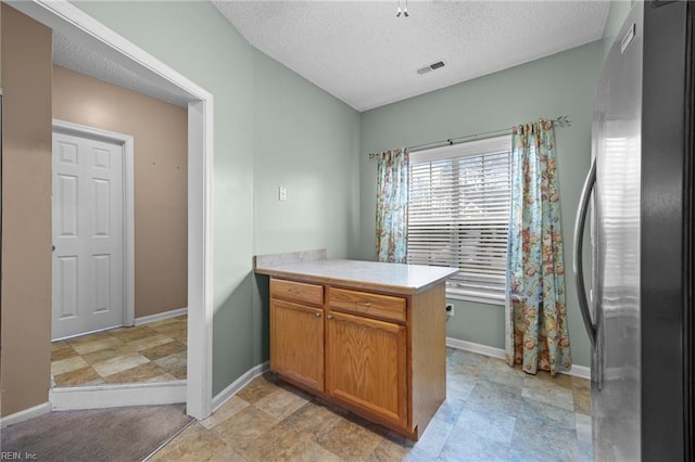 kitchen with a peninsula, visible vents, light countertops, freestanding refrigerator, and brown cabinets