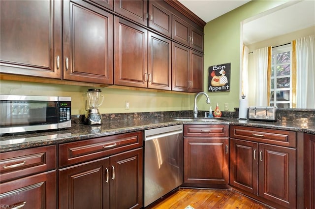 kitchen with dark stone counters, stainless steel appliances, light wood finished floors, and a sink