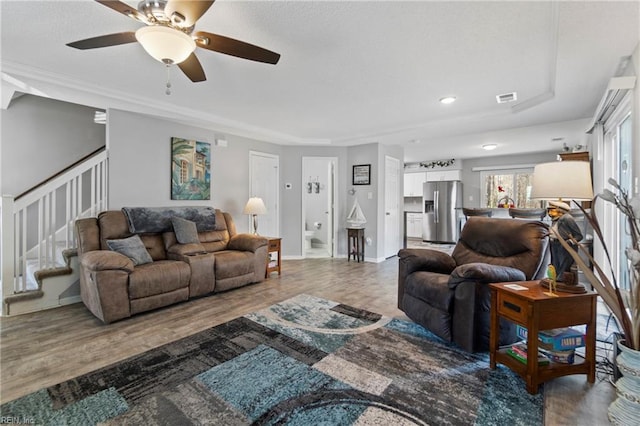 living area with baseboards, visible vents, ceiling fan, stairway, and wood finished floors