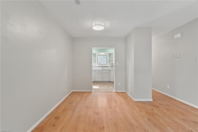 spare room featuring a sink, light wood finished floors, baseboards, and a textured ceiling