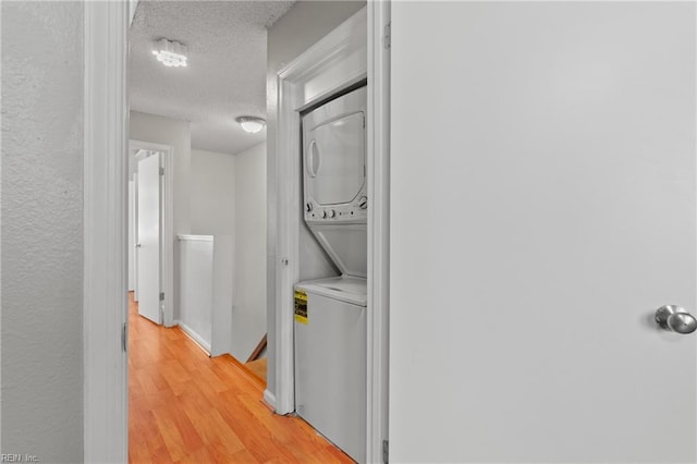 clothes washing area with stacked washer and clothes dryer, a textured ceiling, light wood finished floors, and laundry area