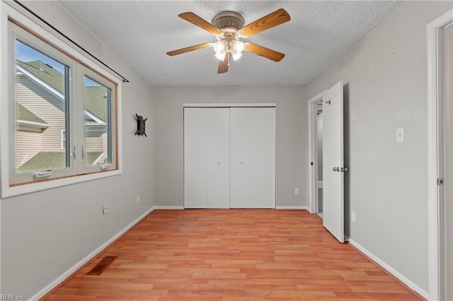 unfurnished bedroom featuring a textured ceiling, visible vents, baseboards, a closet, and light wood-type flooring