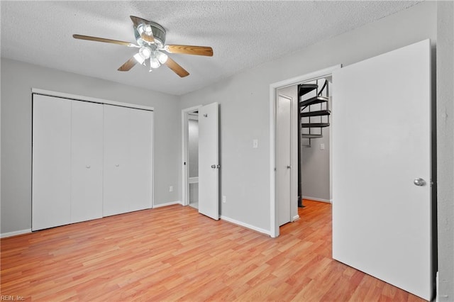 unfurnished bedroom with baseboards, a ceiling fan, a textured ceiling, light wood-style floors, and a closet