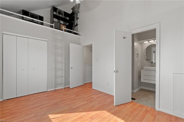 unfurnished bedroom with a closet, a high ceiling, ensuite bath, wood finished floors, and baseboards