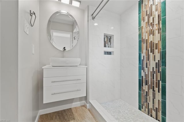 bathroom featuring vanity, baseboards, tiled shower, and wood finished floors